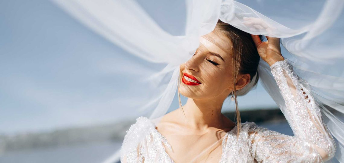 Porträt einer sanften Braut in einem Hochzeitskleid in der Nähe des Flusses an einem sonnigen Tag