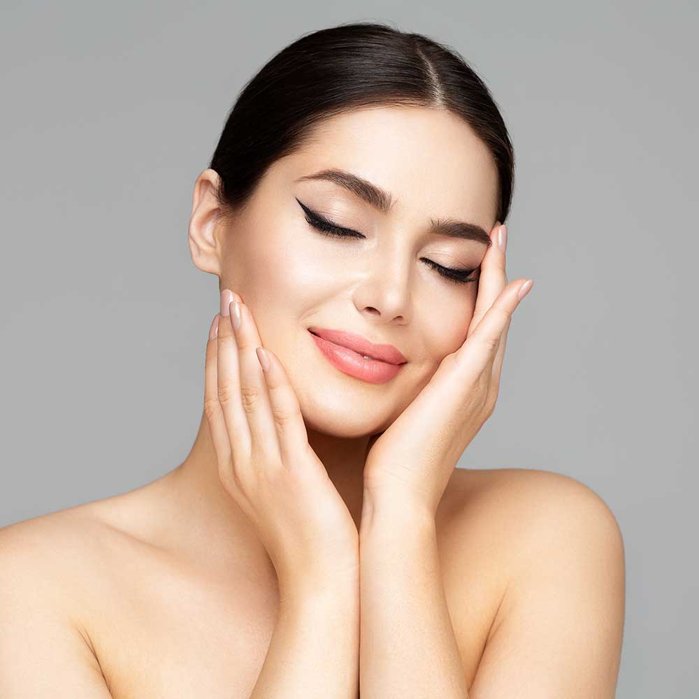 Gesichtspflege für Frauen. Schönheitsmodell, das Gesicht in den Händen hält. Schönes Mädchen mit glatter Haut und prallem Lippen-Make-up über Grau.